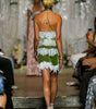 A model viewed from behind walking down a runway wearing a strapless green and white lace mini dress with a halter-style back.
