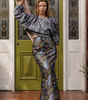Woman in a gray top and floral skirt standing in front of a green door.