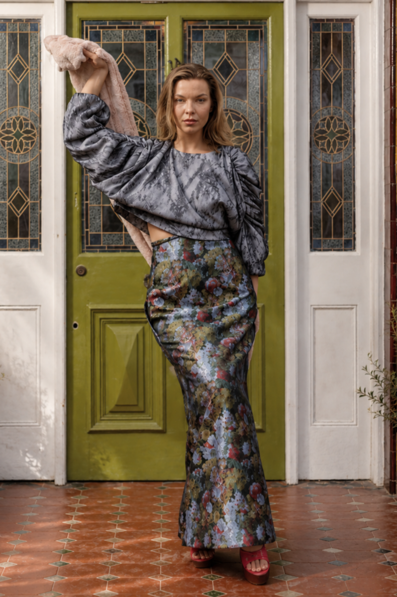 Woman in a gray top and floral skirt standing in front of a green door.