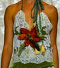 A model walks a fashion runway wearing a halter-neck mini dress made of white lace and green fabric, decorated with a red and yellow floral applique at the bust and a white fringed hem.