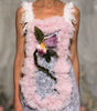 A model walks a fashion runway wearing a light pink and white embellished sleeveless top with a floral applique and matching ruffled cropped pants.