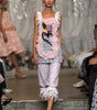 A model walks a fashion runway wearing a light pink and white embellished sleeveless top with a floral applique and matching ruffled cropped pants.
