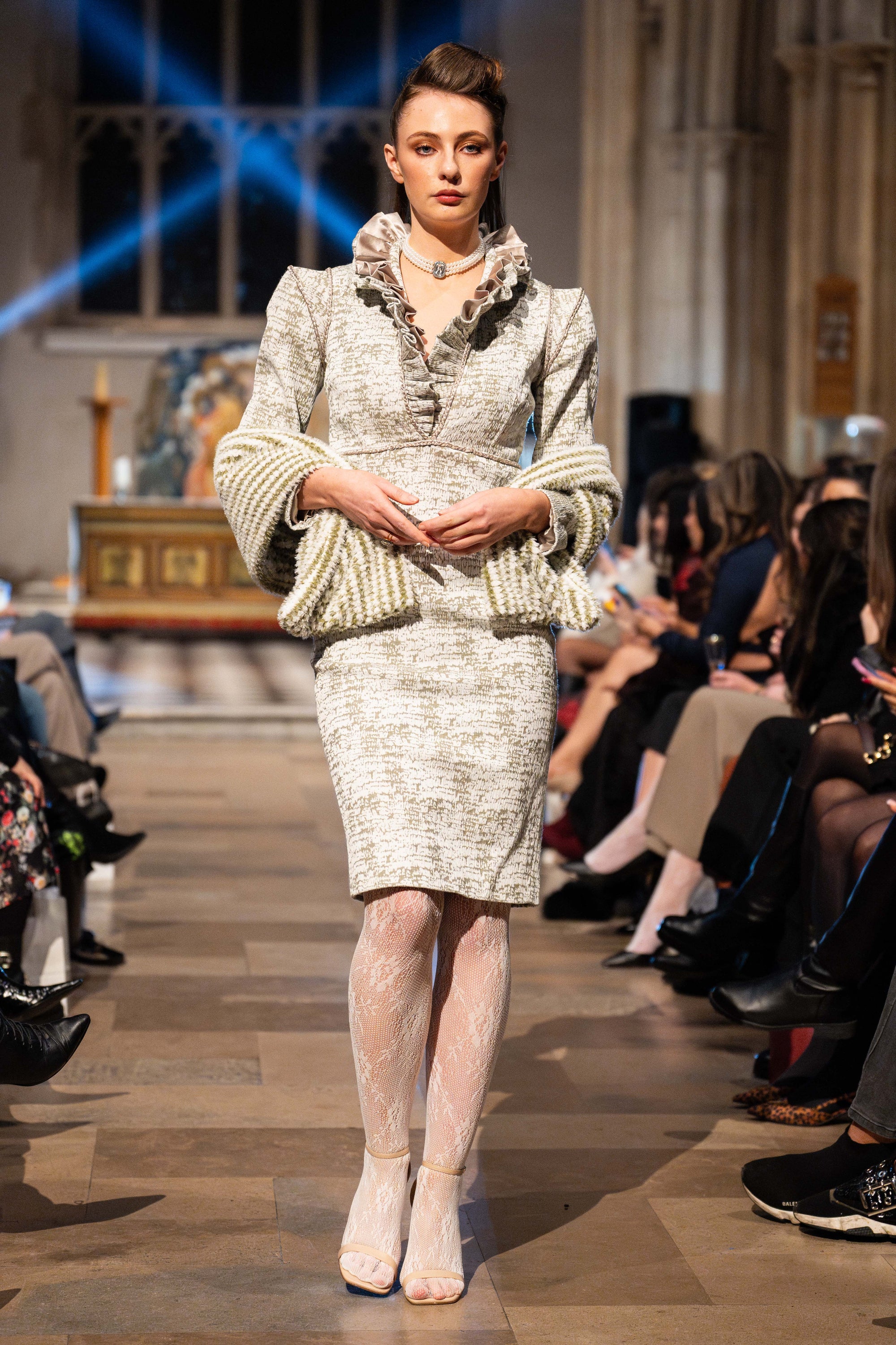 Model walking on a fashion show runway wearing a patterned outfit.