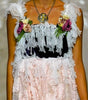 A model walks the runway wearing a sleeveless maxi dress with a black bodice, white floral applique, and a long sheer white skirt with large floral patterns.