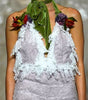 A model walks the runway wearing a textured lavender and white halter jumpsuit with lace ruffle trim and a green neck scarf with floral accents.