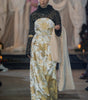 Model walking on a runway wearing a gold and white dress with a black top.