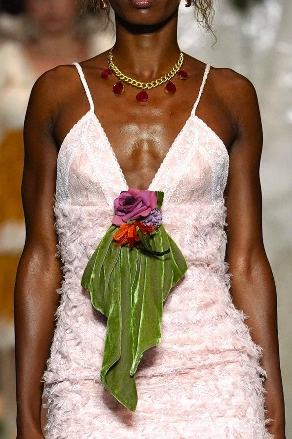 A model walks the runway wearing a light pink ruffled spaghetti-strap dress with sheer wide-leg tulle pants and a green leaf accent at the waist.