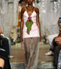 A model walks the runway wearing a light pink ruffled spaghetti-strap dress with sheer wide-leg tulle pants and a green leaf accent at the waist.