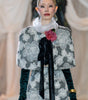 Model walking on a fashion runway wearing a patterned outfit with a floral accessory.