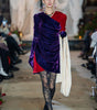 Model walking on a runway wearing a vibrant outfit with purple and red elements.