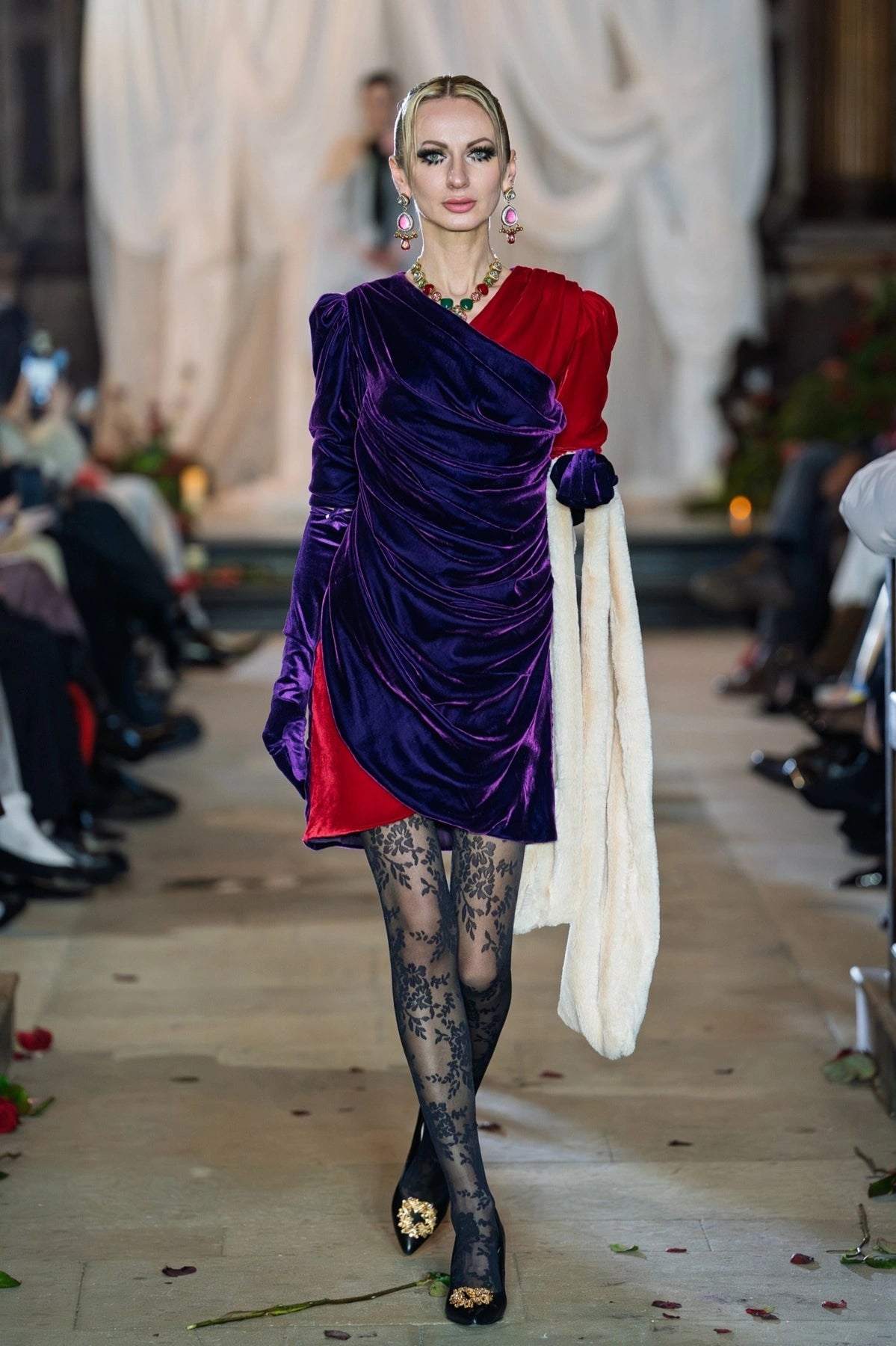 Model walking on a runway wearing a vibrant outfit with purple and red elements.