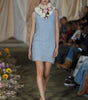 Model wearing a light blue dress with floral accessories on a runway.