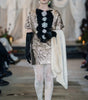 Model on a runway wearing a detailed outfit with floral elements and gloves.