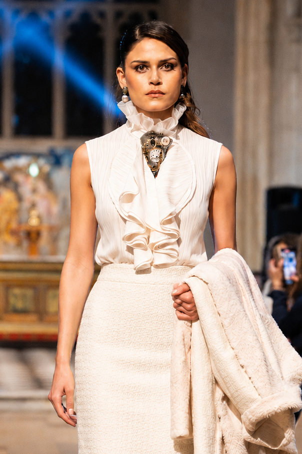 Model walking on a runway wearing a white outfit with a patterned scarf.