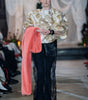 Gold textured jacquard blouse with relaxed silhouette and soft volume styled with sheer lace trousers on runway