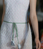Close-up of a white textured dress with a green belt and floral details.