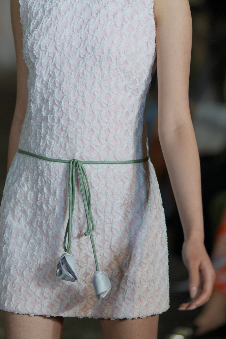 Close-up of a white textured dress with a green belt and floral details.