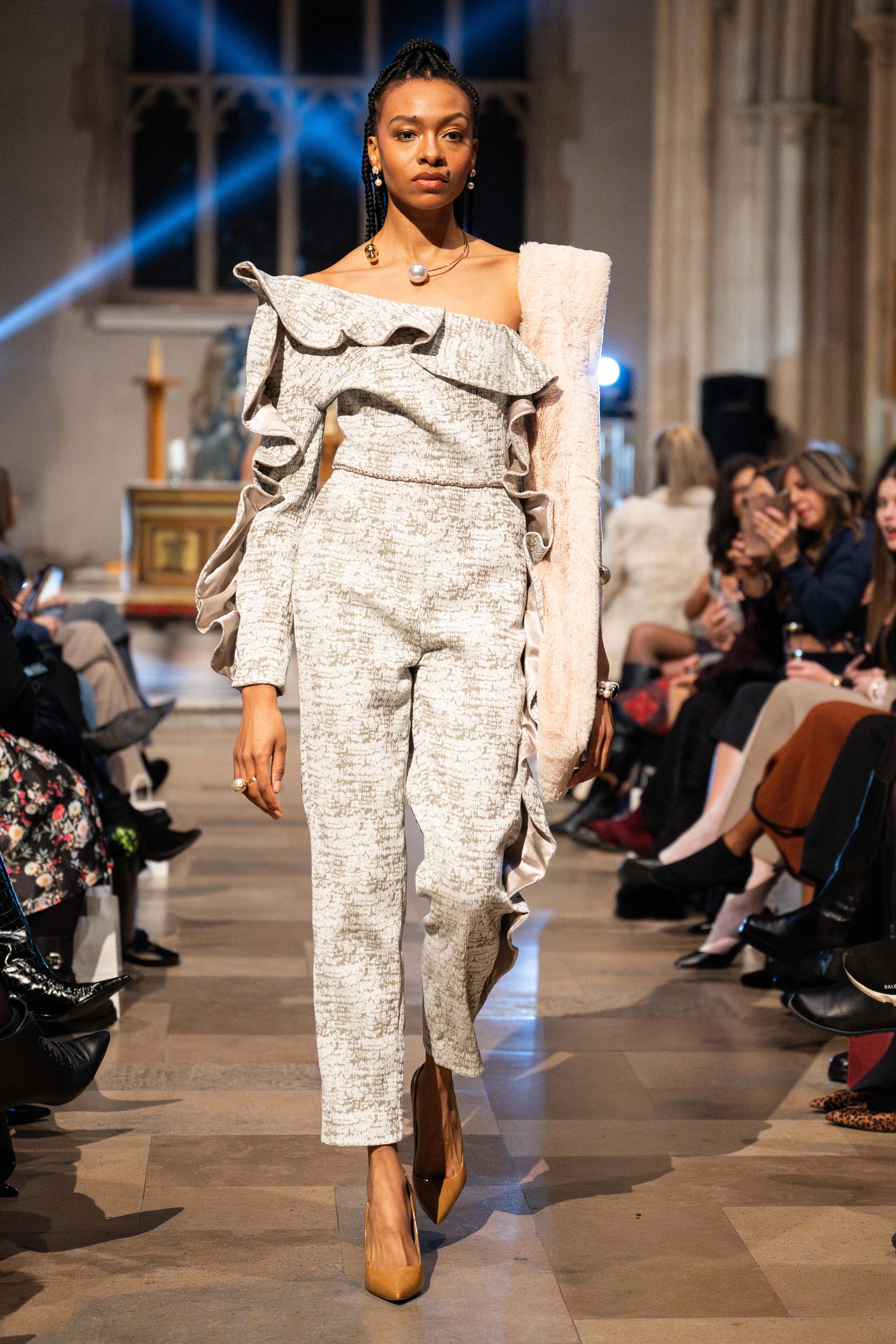 Model walking on a fashion show runway wearing a stylish outfit.