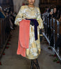 Woman in a floral dress with a pink skirt walking on a catwalk.
