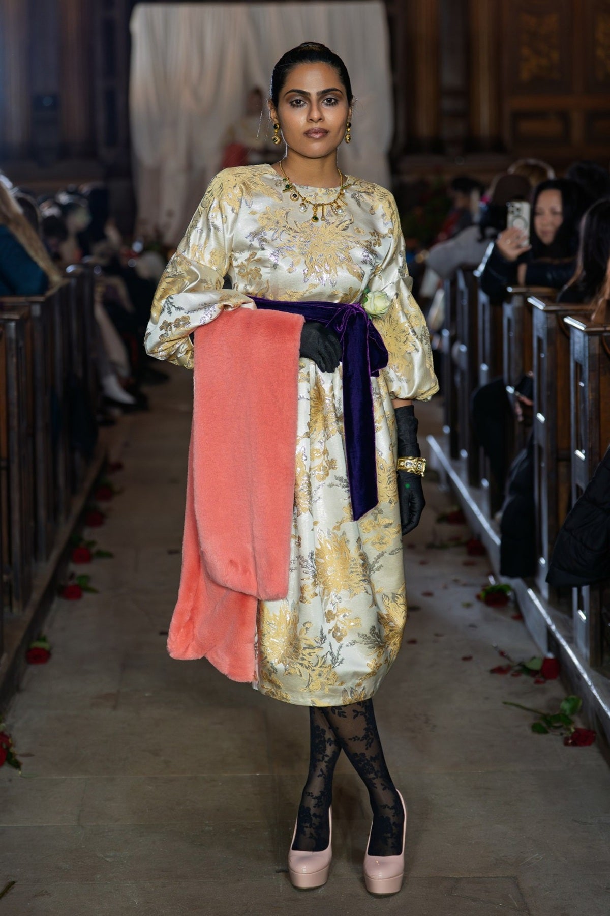 Woman in a floral dress with a pink skirt walking on a catwalk.