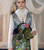 Model walking on a fashion runway wearing a floral dress and patterned vest.