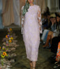 Model walking on a runway wearing a light pink floral dress with a headscarf.