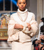 Model walking on a fashion show runway wearing a white outfit with lace details.