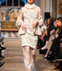 Model walking on a fashion show runway wearing a patterned dress.