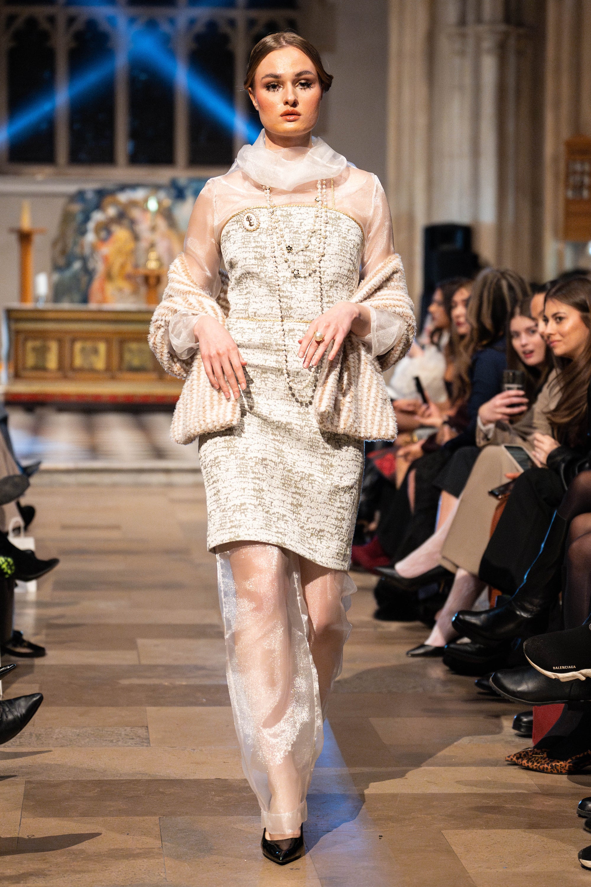 Model walking on a fashion show runway wearing a patterned dress.