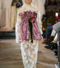 Model wearing a pink sequined top and white lace dress on a runway.