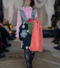 Model walking on a runway wearing a floral dress with a pink shawl.