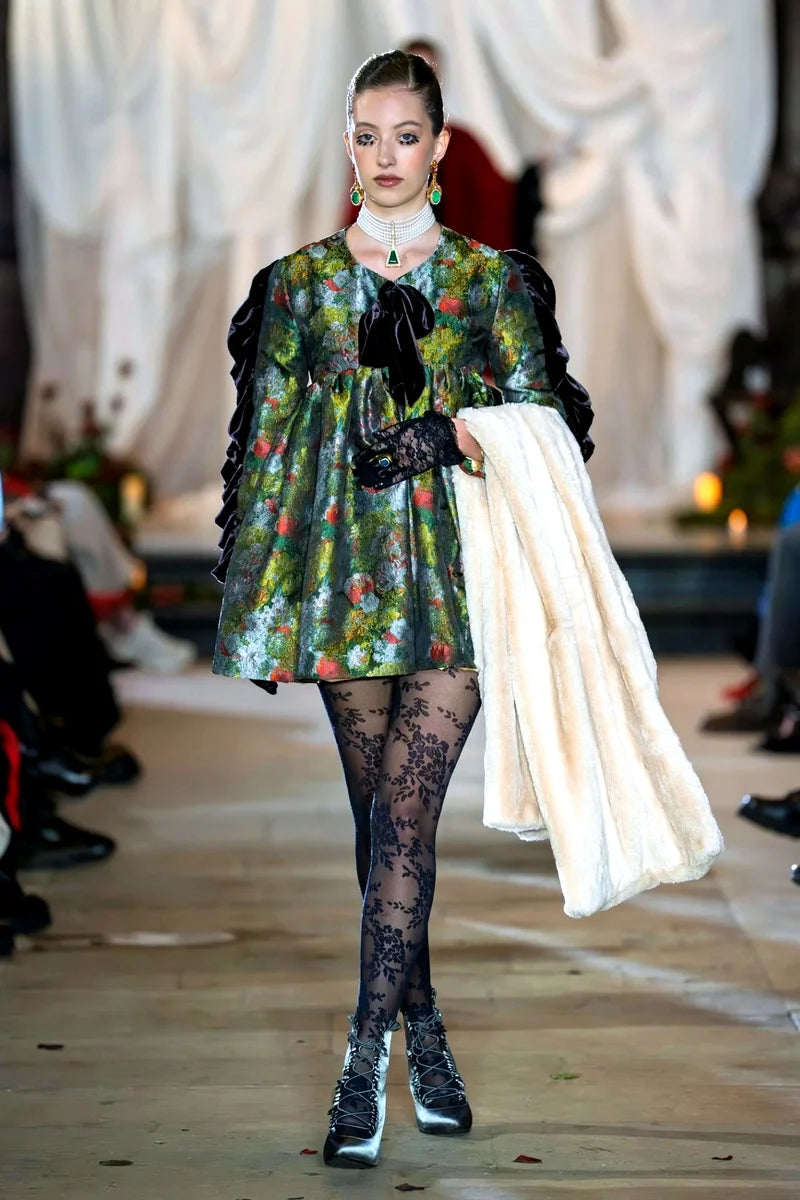 Model walking on a runway wearing a floral dress and black tights.