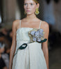 Model wearing a light-colored dress with floral details on a blurred background