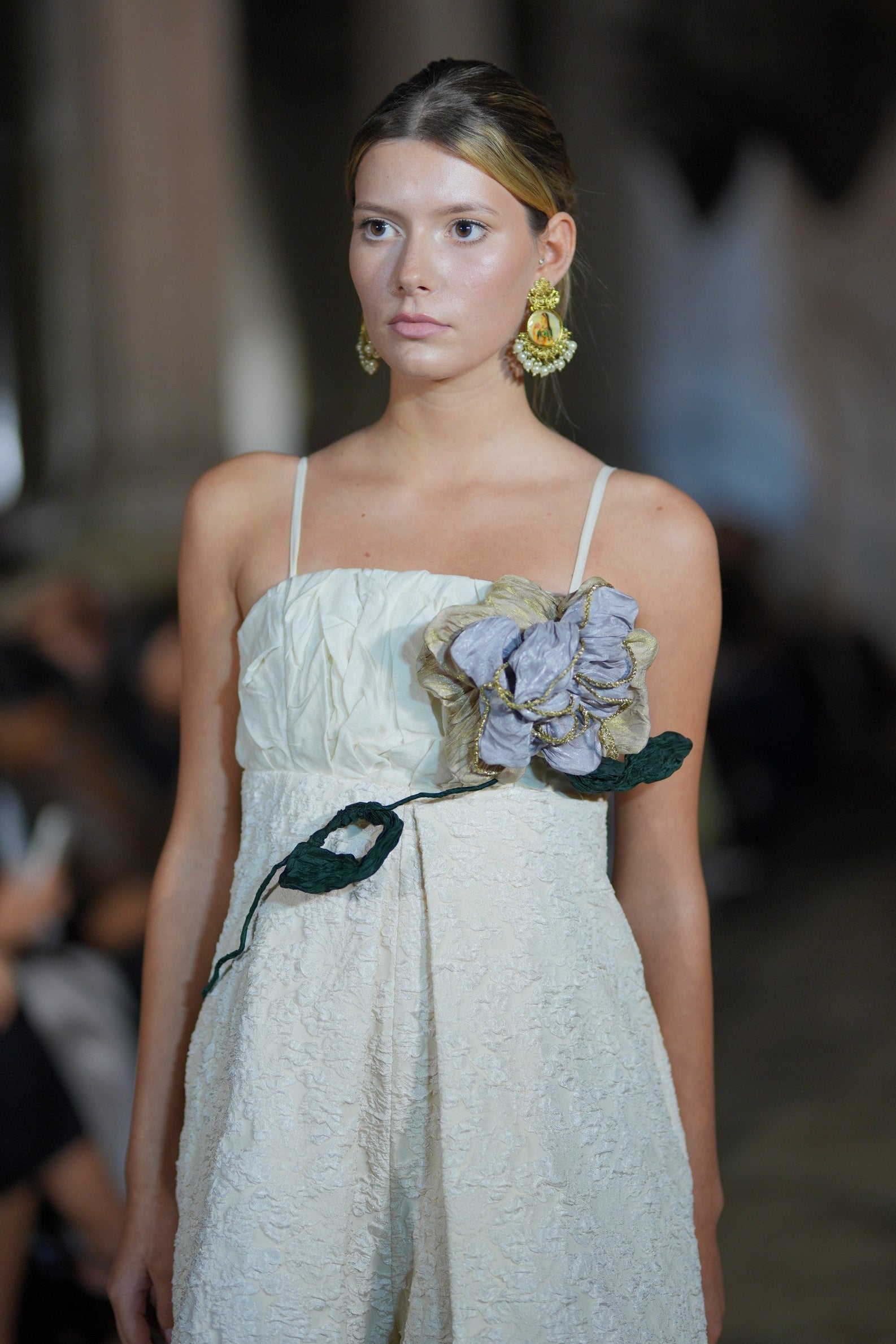 Model wearing a light-colored dress with floral details on a blurred background