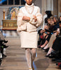 Model walking on a fashion show runway wearing a white outfit with lace details.