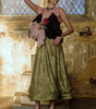 Woman in a vintage-style dress standing in an ornate room with stained glass windows.