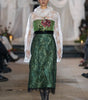 Model wearing a green dress with floral details on a runway