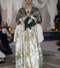 Model wearing a long, elegant dress with gold and white patterns on a runway.