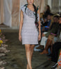 Model walking on a runway wearing a gray dress with ruffled details.