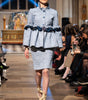 Model walking on a runway wearing a checkered outfit with a peplum top and skirt.