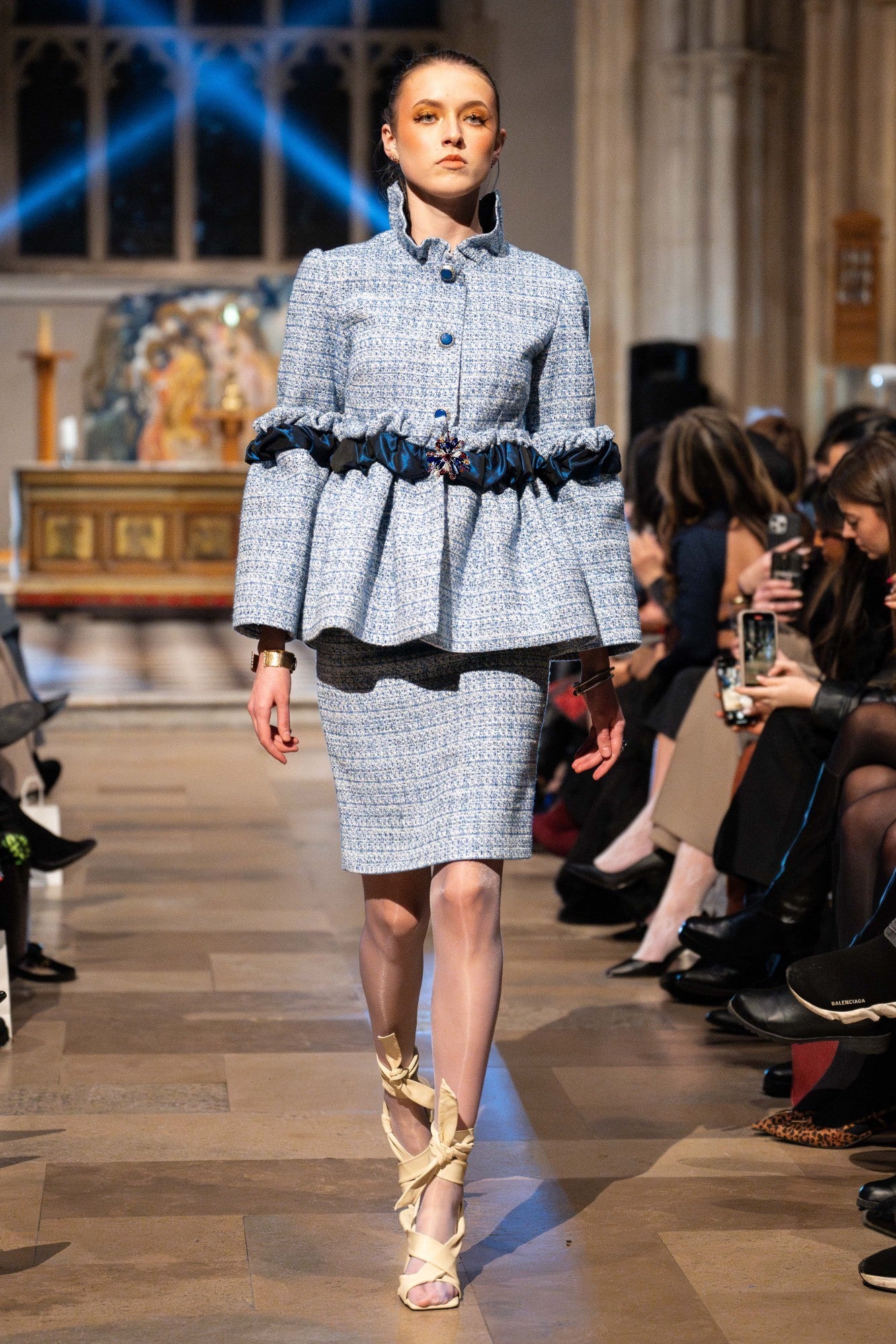 Model walking on a runway wearing a checkered outfit with a peplum top and skirt.