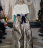 Model wearing a white lace top and patterned pants on a runway with a blurred background