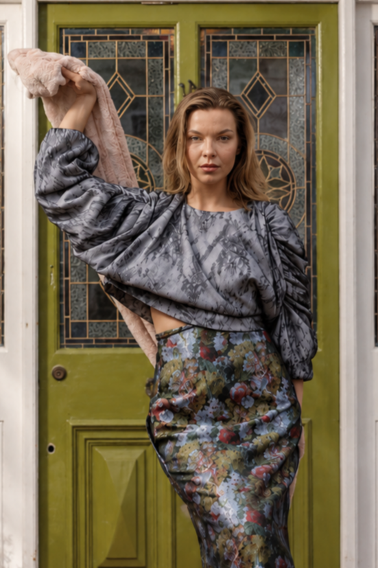 Woman in a gray top and floral skirt standing in front of a green door.