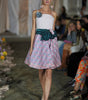 Model walking on a runway wearing a floral dress with a white top and green accents.