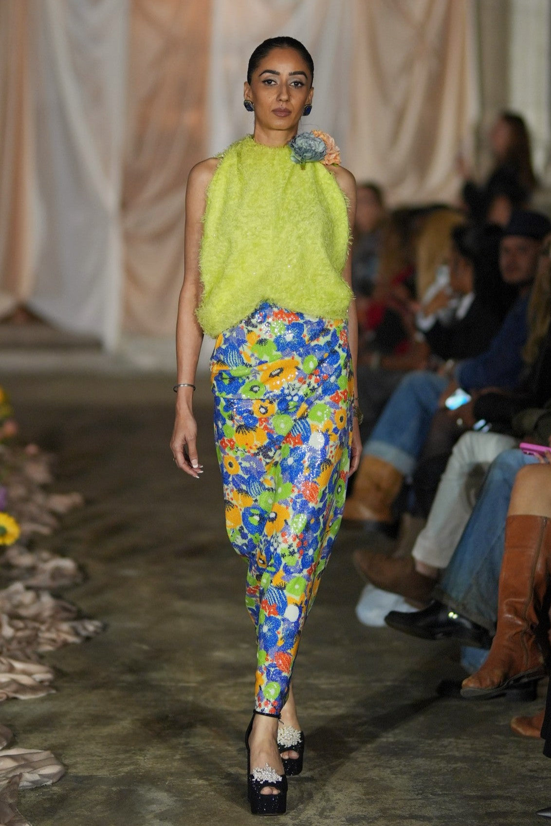 Model wearing a bright green top and colorful pants on a fashion runway.