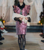 Model wearing a pink sequin dress with black tights and shoes on a runway.