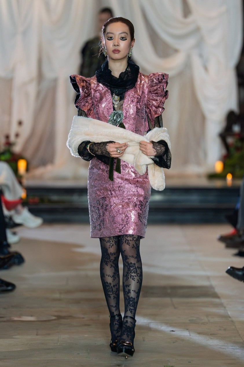 Model wearing a pink sequin dress with black tights and shoes on a runway.