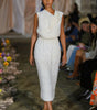 Model wearing a white dress on a runway with an audience in the background