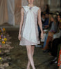 Model walking on a runway wearing a floral dress with a large bow at the front.