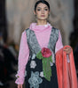 Model wearing a pink blouse with a black floral dress on a runway